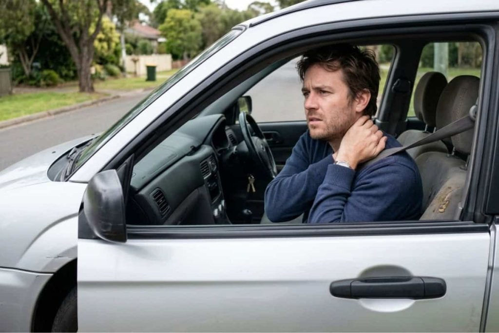 can-i-still-get-compensation-if-i-didnt-go-to-the-er-right-away - Truskett Law Man sits in the driver’s seat of a silver car, clutching his neck in pain.